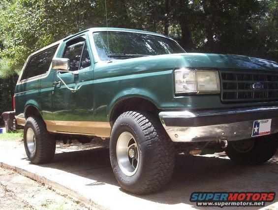 Green Ford Bronco with tan trim, lifted on off-road tires. Texas license plate visible