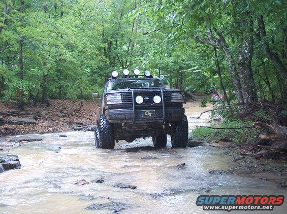 1989 Ford Bronco front view driving through water, with off-road lights and a GT badge