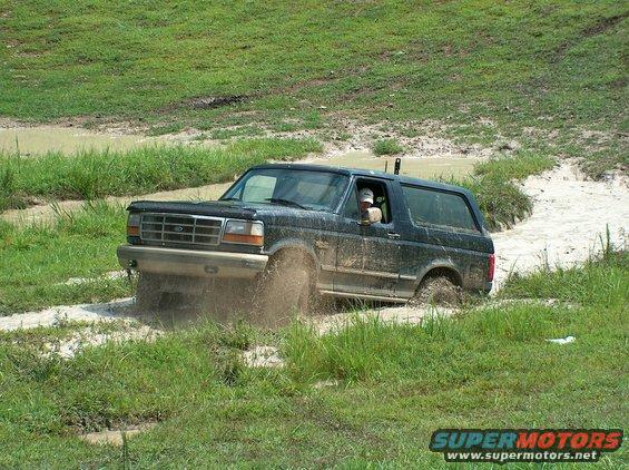 1989 Ford Bronco driving through mud puddle, splashing water