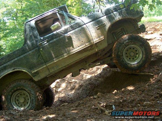 Muddy Ford Bronco climbing a steep, slick hill with trees in the background