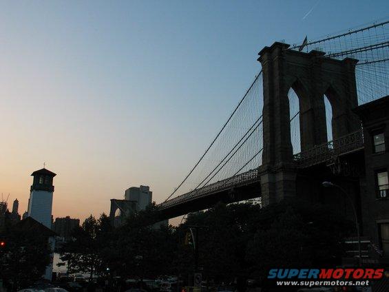 Brooklyn Bridge at dusk with a lighthouse and city skyline