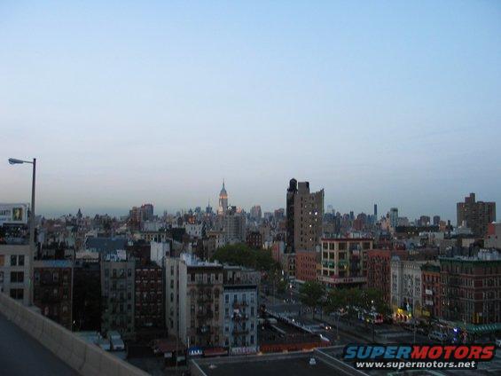 View of NYC buildings with Empire State Building in distance. Streetlights and some cars visible