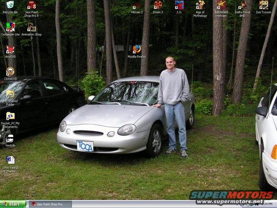 Man standing by a silver 1998 Ford Taurus. Another car is visible to the left, and part of a white vehicle to the right