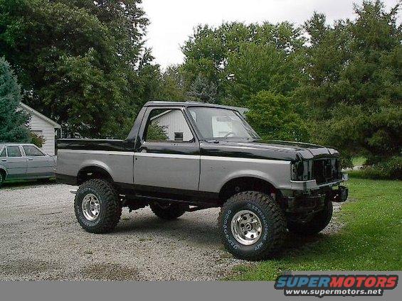 Lifted Ford Bronco with two-tone paint, missing front grille. Side view shows custom wheels and tires