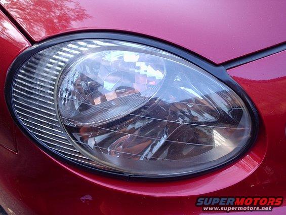 Close-up of a red car's headlight assembly with horizontal grille detail