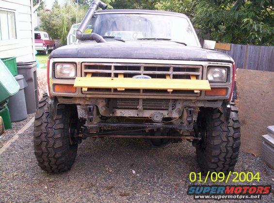Front view of a lifted Ford Bronco with a snorkel. It has large off-road tires and a wooden plank across the grille
