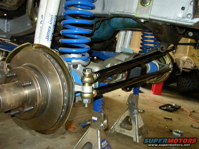 close-up of vehicle suspension with blue coil springs and shocks, brake rotor, and linkage arms