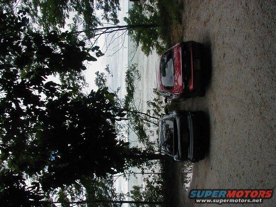 Two cars parked near a body of water, one red and one black