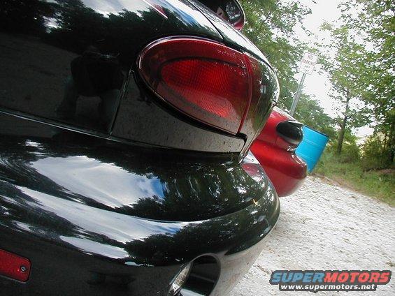 Black Pontiac Sunfire rear end, red car behind it, blue barrel nearby