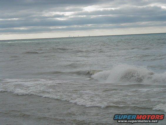 Ocean waves crashing under a cloudy sky with a distant city skyline