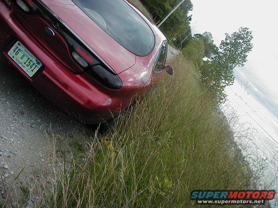 Red Ford Taurus with Indiana license plate 46 D 1541 parked on a gravel shoulder with tall grass