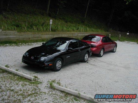 Black coupe and red sedan parked on gravel lot