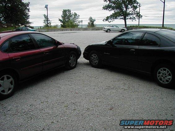 Two cars parked facing each other on a gravel lot near a body of water