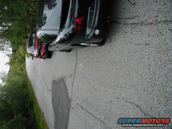 Rear view of a black car and a red car parked on a cracked asphalt road with trees in the background