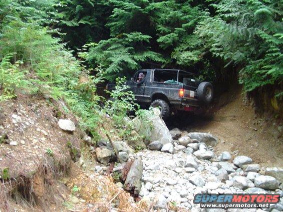 Black 1993 Ford Bronco driving on a rocky, wooded trail