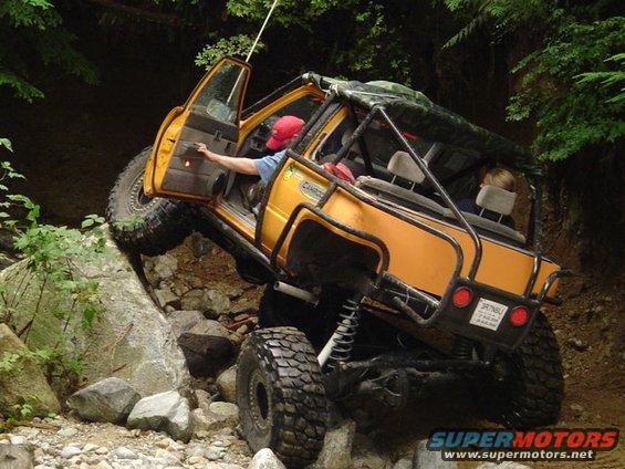 Yellow off-road vehicle with open door, climbing over rocks on a dirt trail