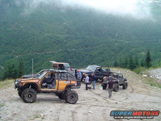 Several off-road vehicles parked on a dirt path with a forested mountain in the background