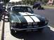 1968 Ford Mustang - A green 1968 Ford Mustang with white racing stripes is parked on the street, with other vehicles visible in the background.