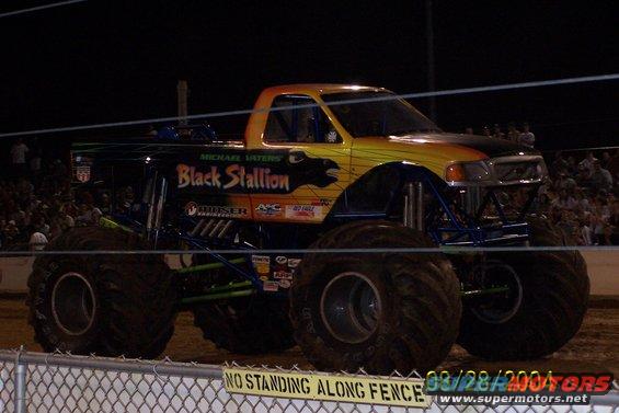 Monster truck with 'Black Stallion' graphics and large tires sits in front of a crowd