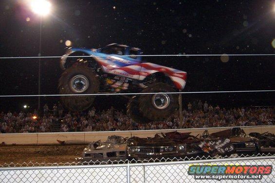 Monster truck with American flag paint scheme jumping over crushed cars