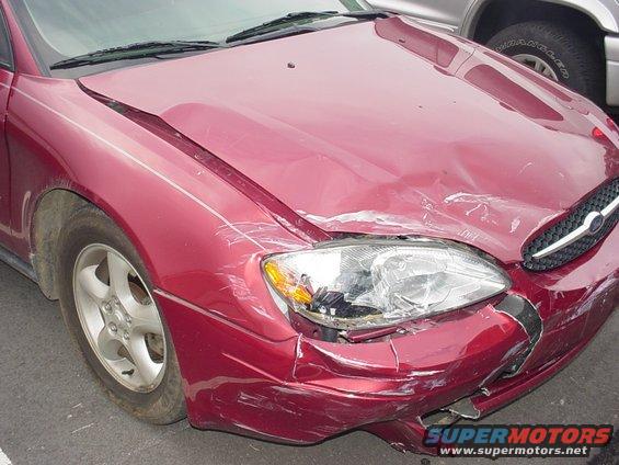 Maroon Ford sedan with crumpled hood, broken right headlight and damaged front bumper from a collision