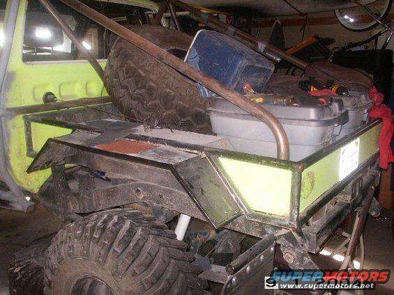 Yellow truck bed with large spare tire, grey storage boxes, and metal roll cage. Some parts appear unpainted