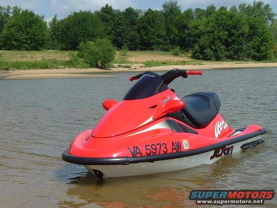 Red jet ski with registration VA 5973 AW parked in shallow water near a sandy shore with trees in the background