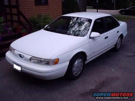 White Ford sedan parked in a driveway. It has a blue oval Ford emblem on the front