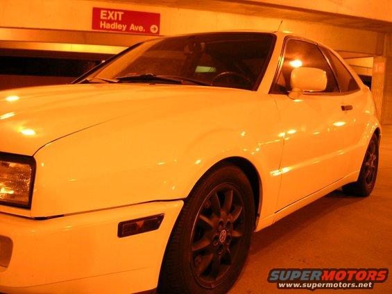 White Volkswagen Corrado, front 3/4 view, parked indoors. Visible: headlight, fender, door, wheel, side mirror