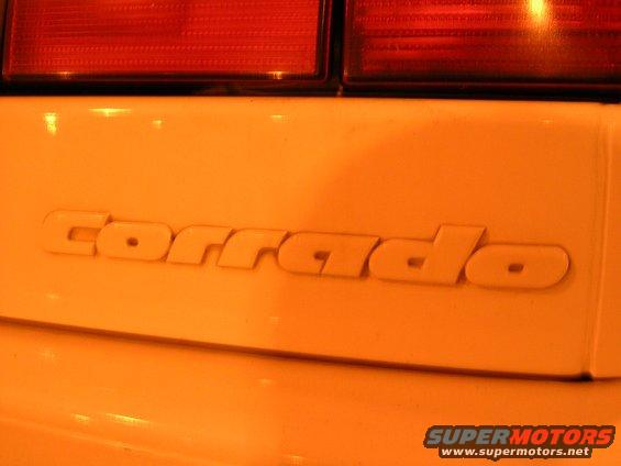 Close-up of 'corrado' emblem on a yellow car, with red taillights visible above
