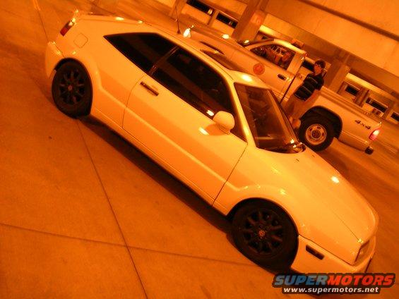 White 1990 Volkswagen Corrado coupe with black wheels, parked indoors. The car is viewed from the front three-quarter angle