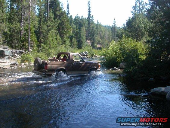 Brown 1990 Ford Bronco driving through a river, side view