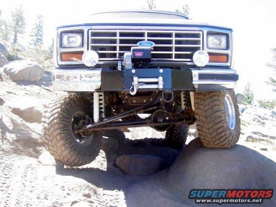 Front view of a lifted Ford Bronco with a winch mounted on the bumper, driving over rocks