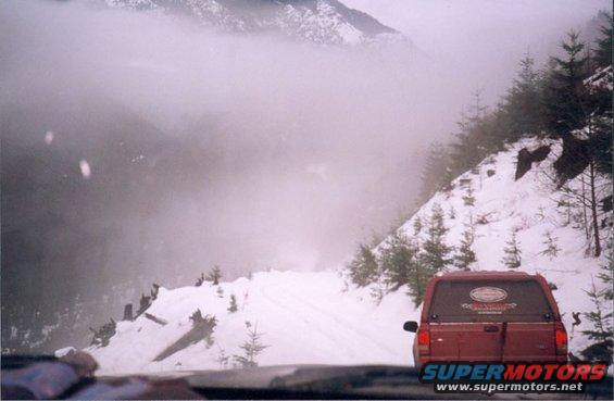 Red SUV on a snowy mountain road with fog in the background