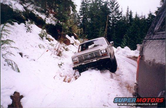 1980s Ford Bronco driving on a snowy road, partially off-road