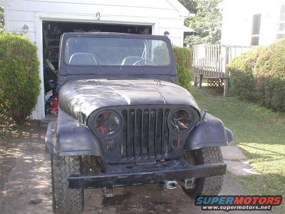 Front view of a dark-colored Jeep CJ-5 parked in front of a garage