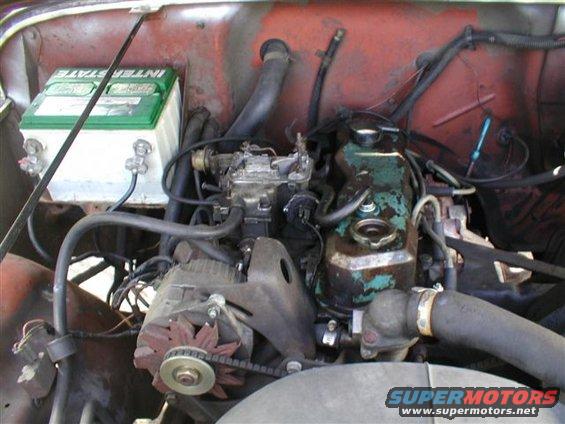 Engine bay with Interstate battery, carburetor, and alternator. Red painted firewall