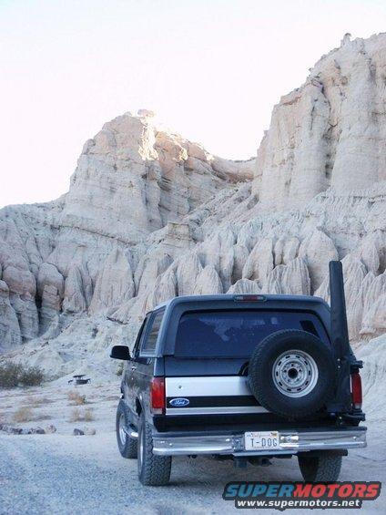 Black Ford Bronco with spare tire on rear, parked on dirt road near rock formations