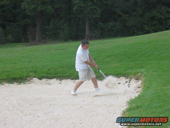 Golfer in sand trap, kicking up sand with club
