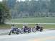 1995 Mercury Grand Marquis - Three motorcycles are parked on the side of a road with a grassy hillside behind them.