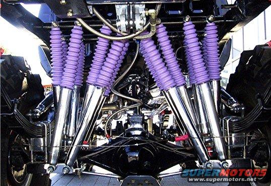 Underside view of a vehicle's rear suspension with multiple chrome shocks and purple bellows