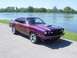 1978 Ford Mustang II - This 1978 Ford Mustang II coupe, painted in a striking purple hue, features a prominent hood scoop and is captured in a three-quarter front…