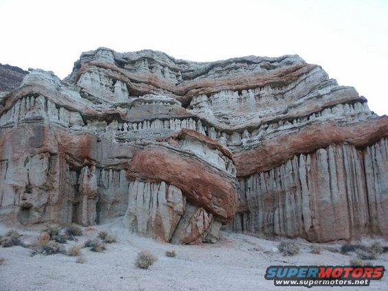layered red and white rock formations with sparse desert brush