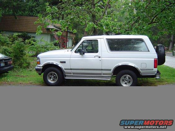 White 1992 Ford Bronco parked on a grassy area next to a house. Side view