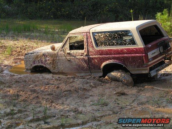 Mud-covered 1989 Ford Bronco stuck deep in a muddy ditch