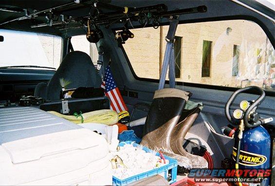 1996 Ford Bronco interior with fishing rods, boots, cooler, and air tank