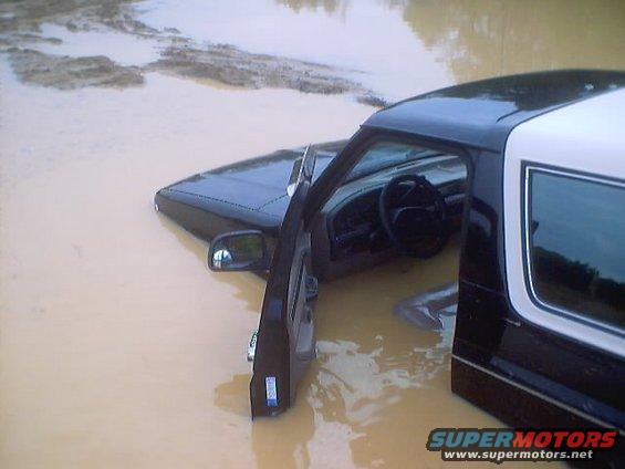 1995 Ford Bronco partially submerged in muddy water, driver's door open
