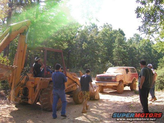 Muddy SUV and backhoe on a dirt road with trees around