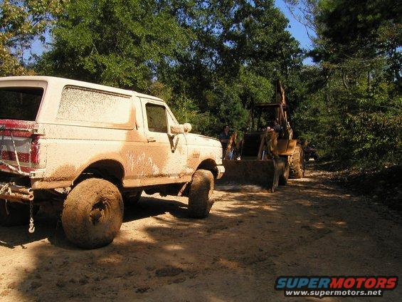Mud-covered 1989 Ford Bronco parked next to a backhoe on a dirt road