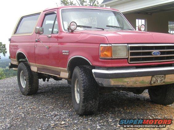 1989 Ford Bronco, red with tan trim, parked on gravel